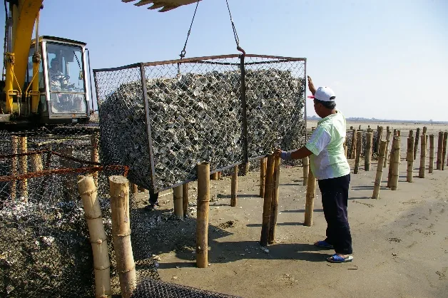 Excavator placing a gabion unit on the beach